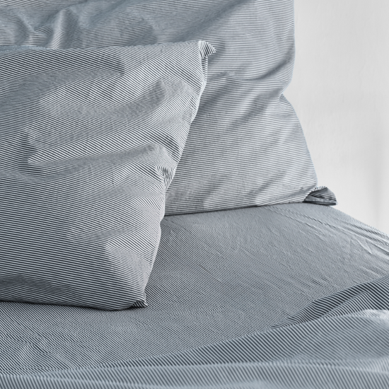 Close-up of blue striped bedding with pillows on a bed. 100% Organic percale cotton bed sheets. 