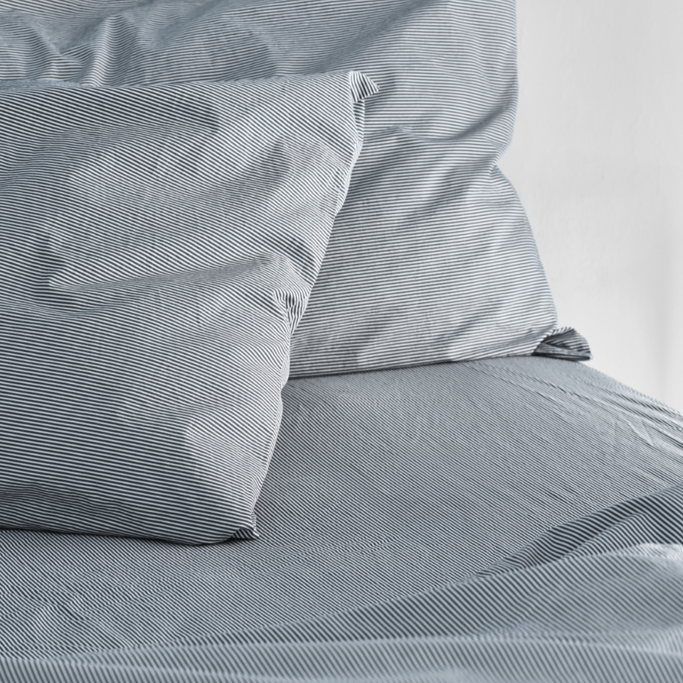 Close-up of blue striped bedding with pillows on a bed. 100% Organic percale cotton bed sheets. 