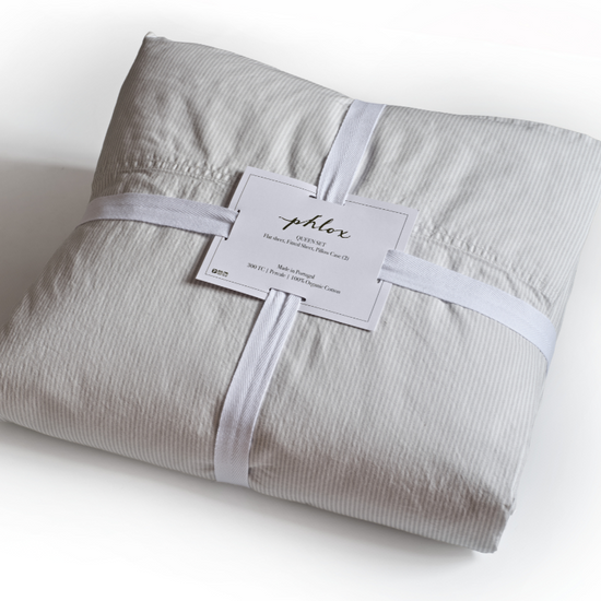 Folded gray striped fabric with a label on a white background. 100% Organic percale cotton bed sheets. 