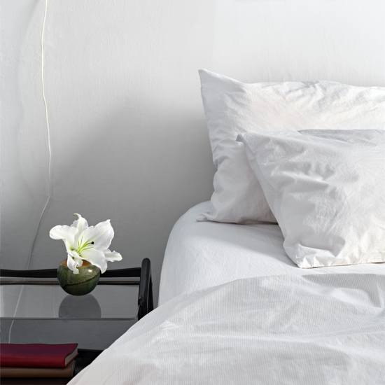White striped bedding with a flower on a nightstand in a bedroom setting. 100% Organic percale cotton bed sheets. 