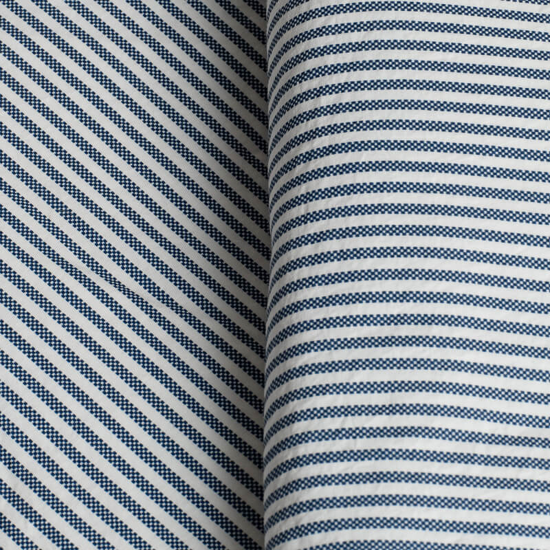 Close-up of fabric with blue and white striped pattern. 100% Organic percale cotton bed sheets. 