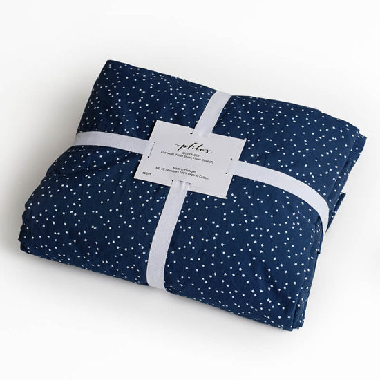 Folded navy blue fabric with white polka dots and a visible brand label on a white background. 100% Organic percale cotton bed sheets. 