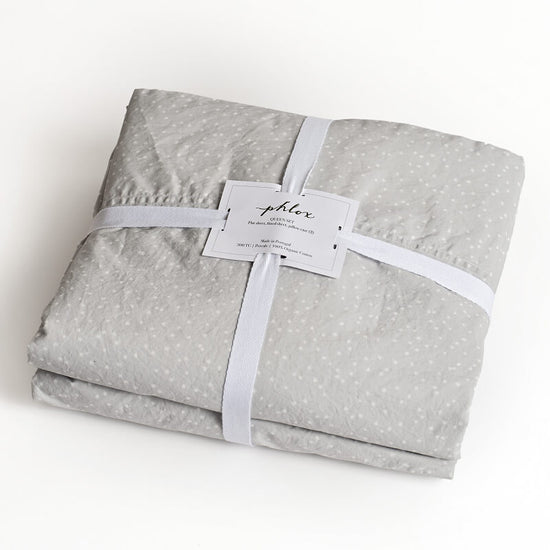Folded gray fabric with white stars and a white ribbon on a white background, branded 'phlox'. 100% Organic percale cotton bed sheets. young girl bedroom sheets. 